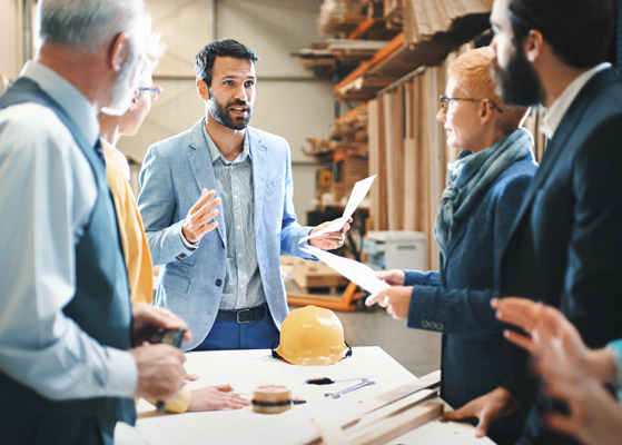 Several male and female engineers standing around a table discussing a business deal