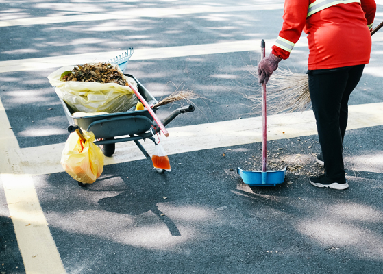Person sweeping up dirt and leaves in a parking lot